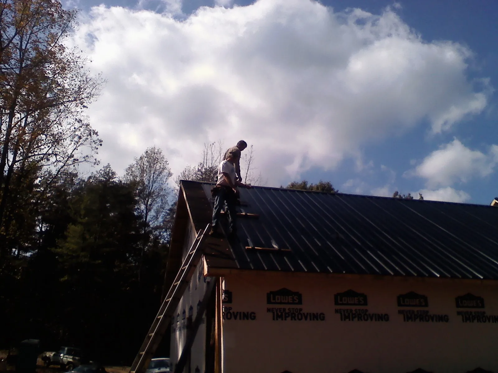 Roofer fastening dark metal panels high against a cloudy sky, from a Roof Inspection job in Murray